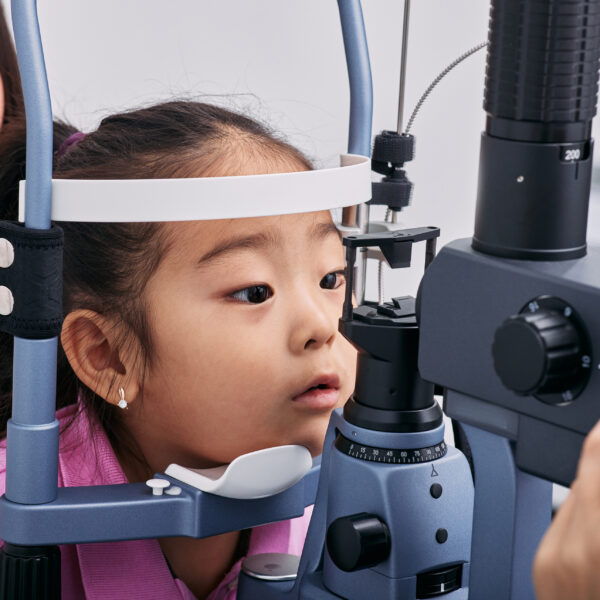 Checking little girl's eyesight with binocular slit lamp in ophthalmology clinic, close-up. Vision correction in children