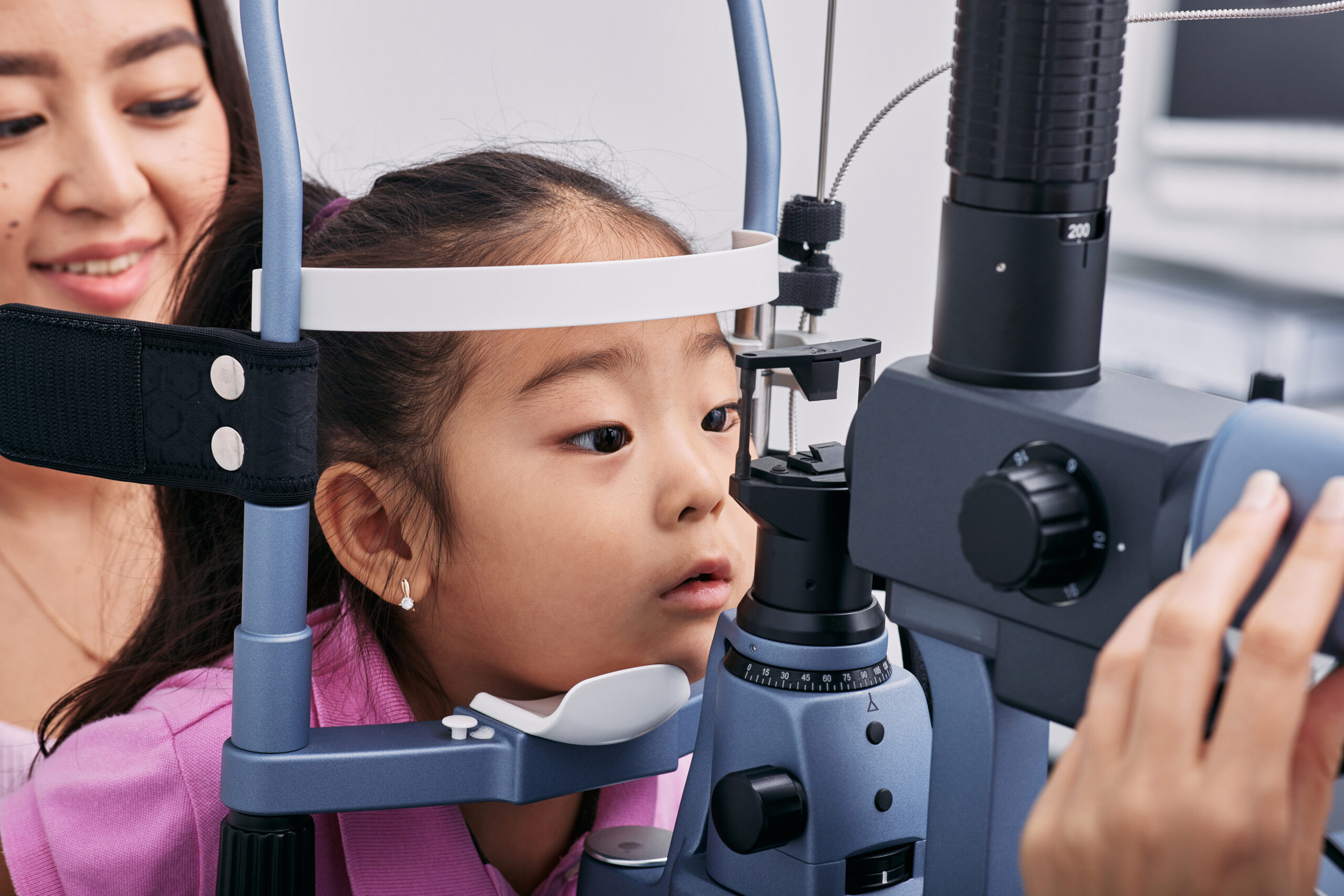 Checking little girl's eyesight with binocular slit lamp in ophthalmology clinic, close-up. Vision correction in children